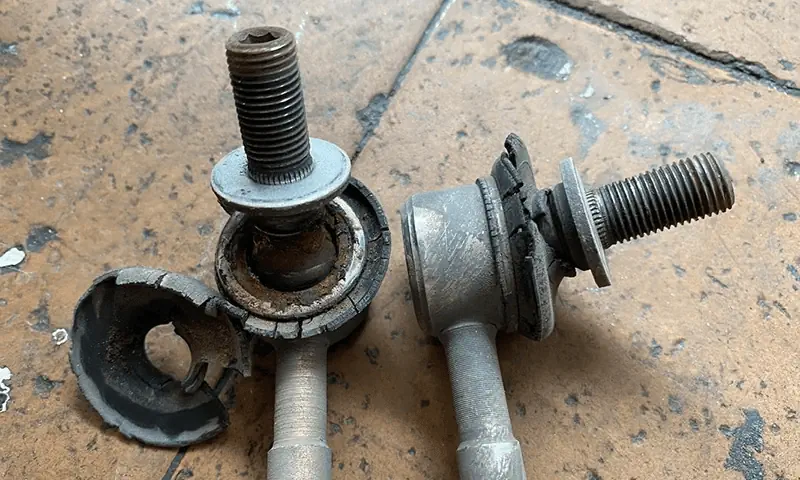 Two severely worn sway bar links showing ball‑joint wear and bushing damage